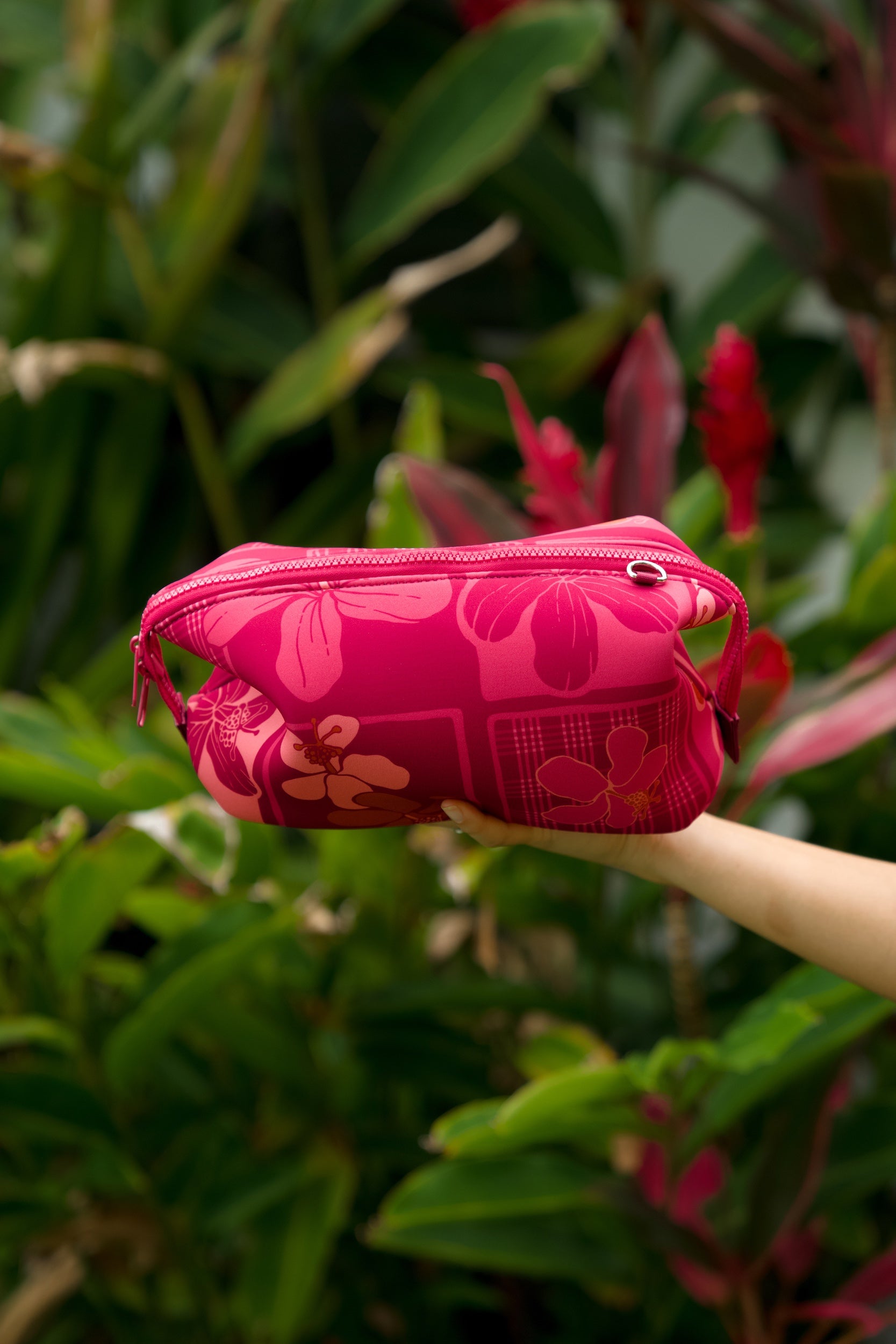 woman holding an expandable neoprene travel pouch with palaka and kokio print