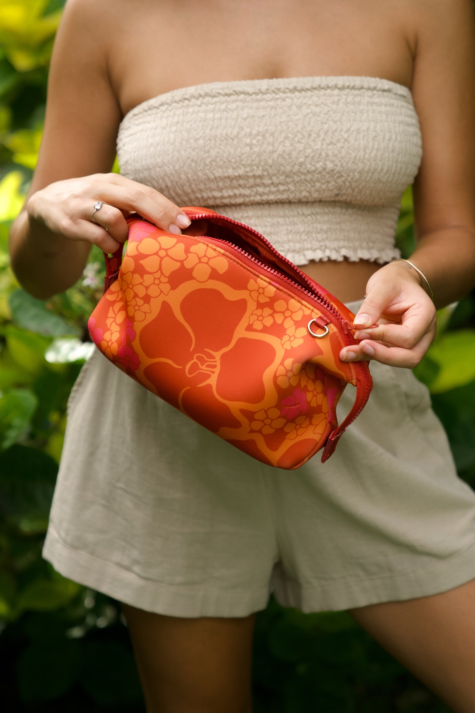 woman holding expandable puakenikeni printed neoprene pouch with detachable mini pouches