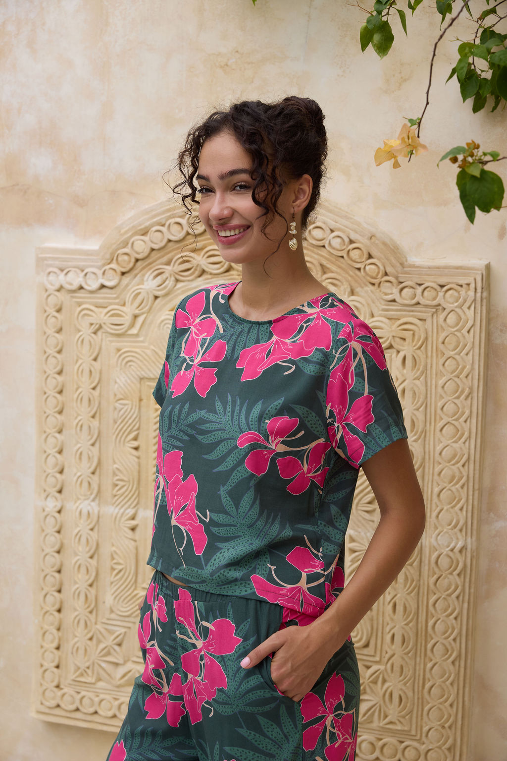 woman with brown hair wearing dark green boxy t-shirt blouse with button-back closure, with fern and ginger print