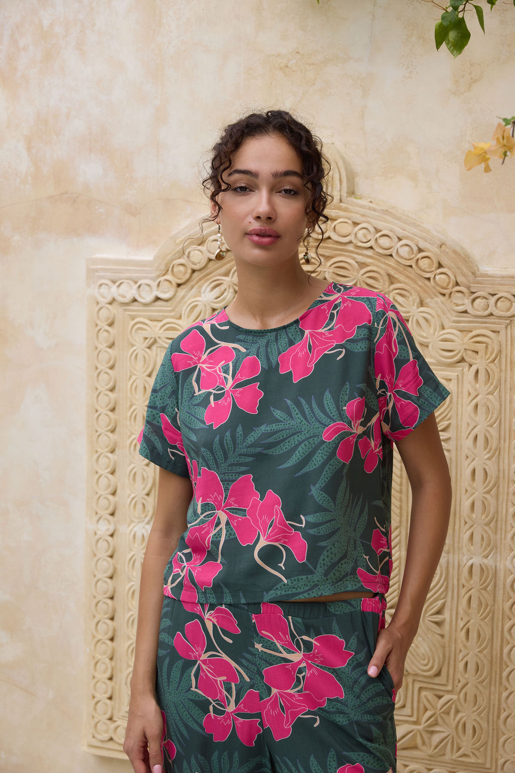 woman with brown hair wearing dark green boxy t-shirt blouse with button-back closure, with fern and ginger print