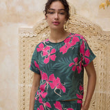woman with brown hair wearing dark green boxy t-shirt blouse with button-back closure, with fern and ginger print