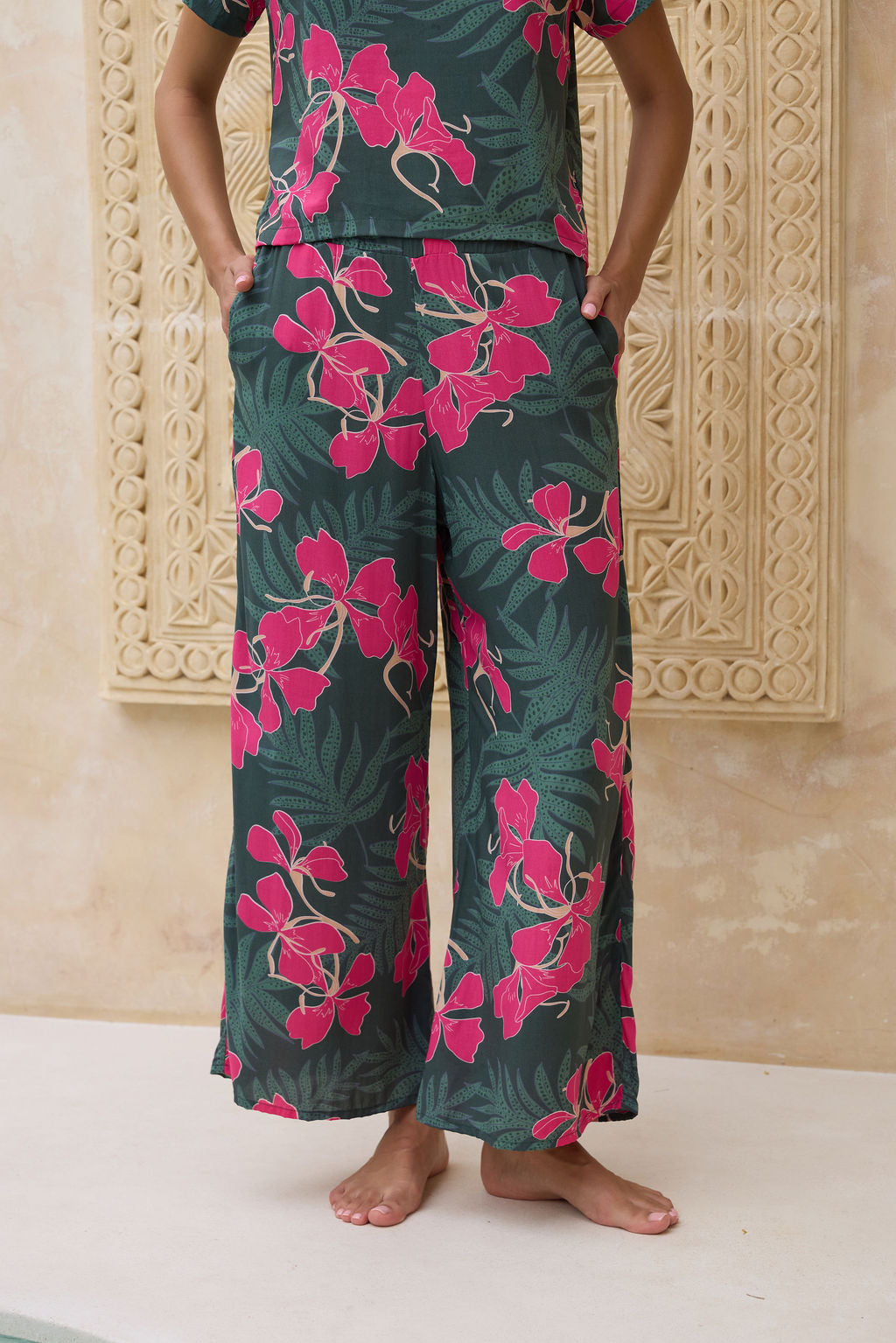 woman with brown hair wearing dark green flowy pants with fern and ginger print