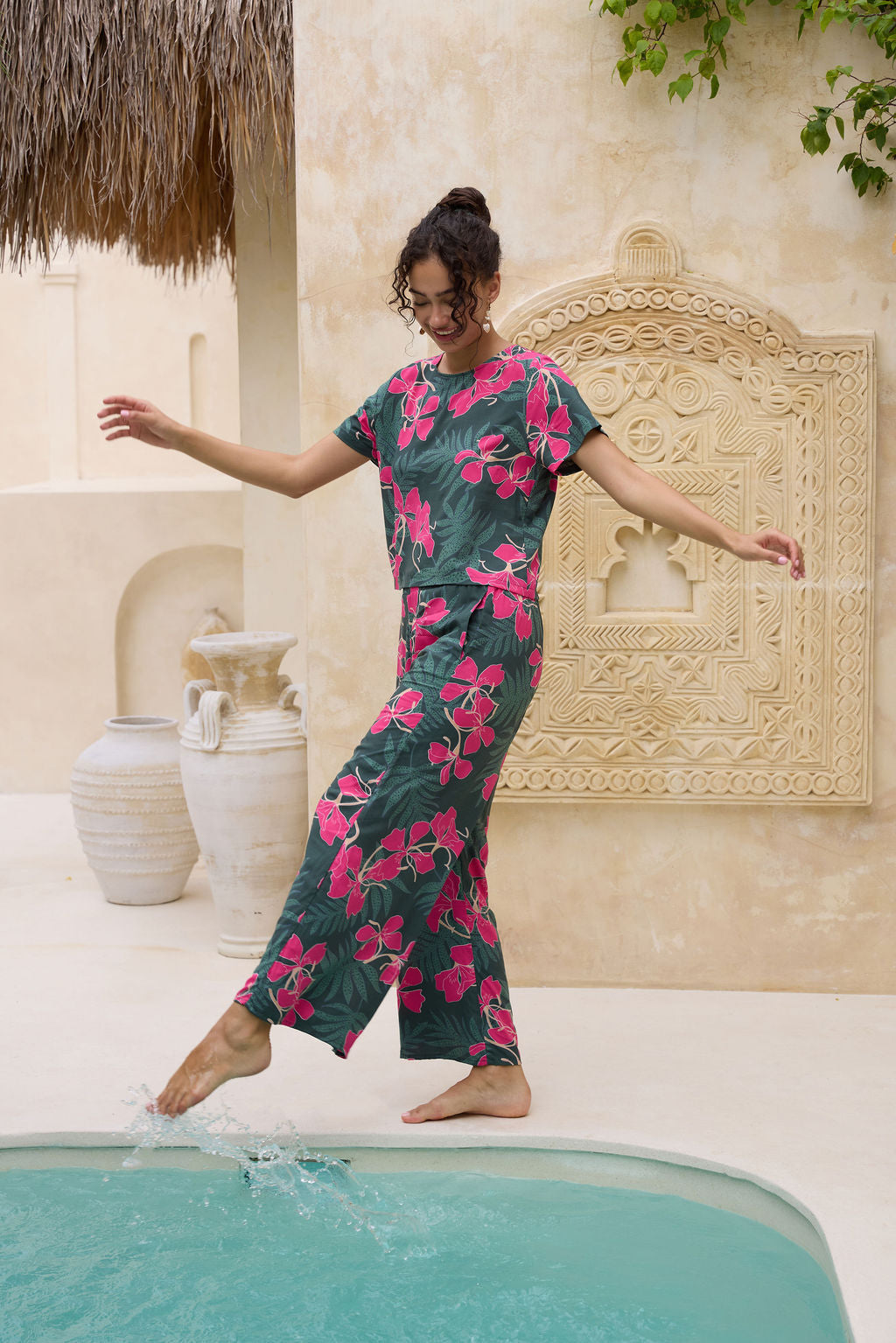 woman with brown hair wearing dark green flowy pants with fern and ginger print