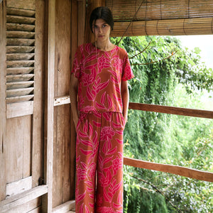 A woman with dark hair wears a YIREH t-shirt top with shell button back. It is the Noe Top in the Garden 'Awapuhi print. 