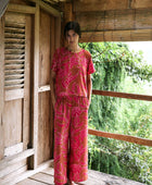 A woman with dark hair wears a YIREH t-shirt top with shell button back. It is the Noe Top in the Garden 'Awapuhi print. 