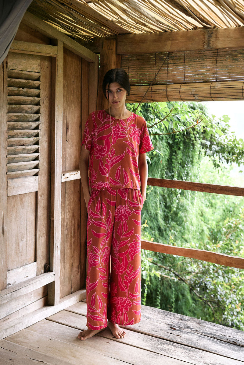 A woman with dark hair wears a YIREH t-shirt top with shell button back. It is the Noe Top in the Garden 'Awapuhi print. 