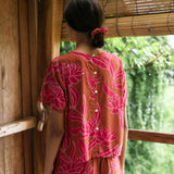 A woman with dark hair wears a YIREH t-shirt top with shell button back. It is the Noe Top in the Garden 'Awapuhi print. 