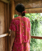 A woman with dark hair wears a YIREH t-shirt top with shell button back. It is the Noe Top in the Garden 'Awapuhi print. 