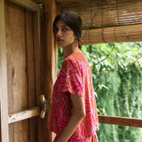 A woman with dark hair wears a YIREH t-shirt top with shell button back. It is the Noe Top in the Garden 'Awapuhi print. 