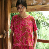 A woman with dark hair wears a YIREH t-shirt top with shell button back. It is the Noe Top in the Garden 'Awapuhi print. 