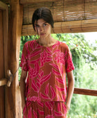 A woman with dark hair wears a YIREH t-shirt top with shell button back. It is the Noe Top in the Garden 'Awapuhi print. 