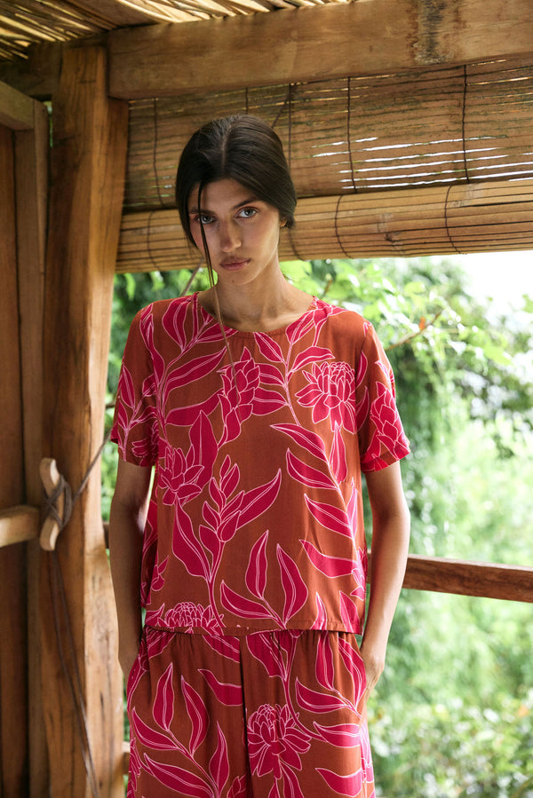 A woman with dark hair wears a YIREH t-shirt top with shell button back. It is the Noe Top in the Garden 'Awapuhi print. 