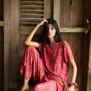 A woman with dark hair wears a YIREH t-shirt top with shell button back. It is the Noe Top in the Garden 'Awapuhi print. 