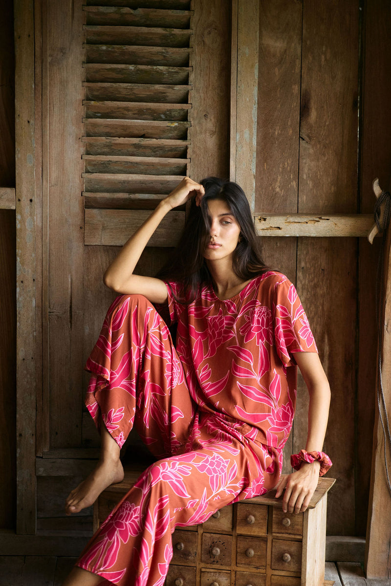 A woman with dark hair wears a YIREH t-shirt top with shell button back. It is the Noe Top in the Garden 'Awapuhi print. 