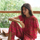 A woman with dark hair wears a YIREH t-shirt top with shell button back. It is the Noe Top in the Garden 'Awapuhi print. 