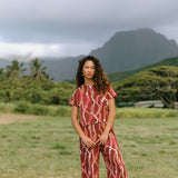 woman with brown hair wearing red-brown colored pant and top with button closure back and lei print