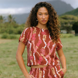 woman with brown hair wearing red-brown colored top with button closure back and lei print