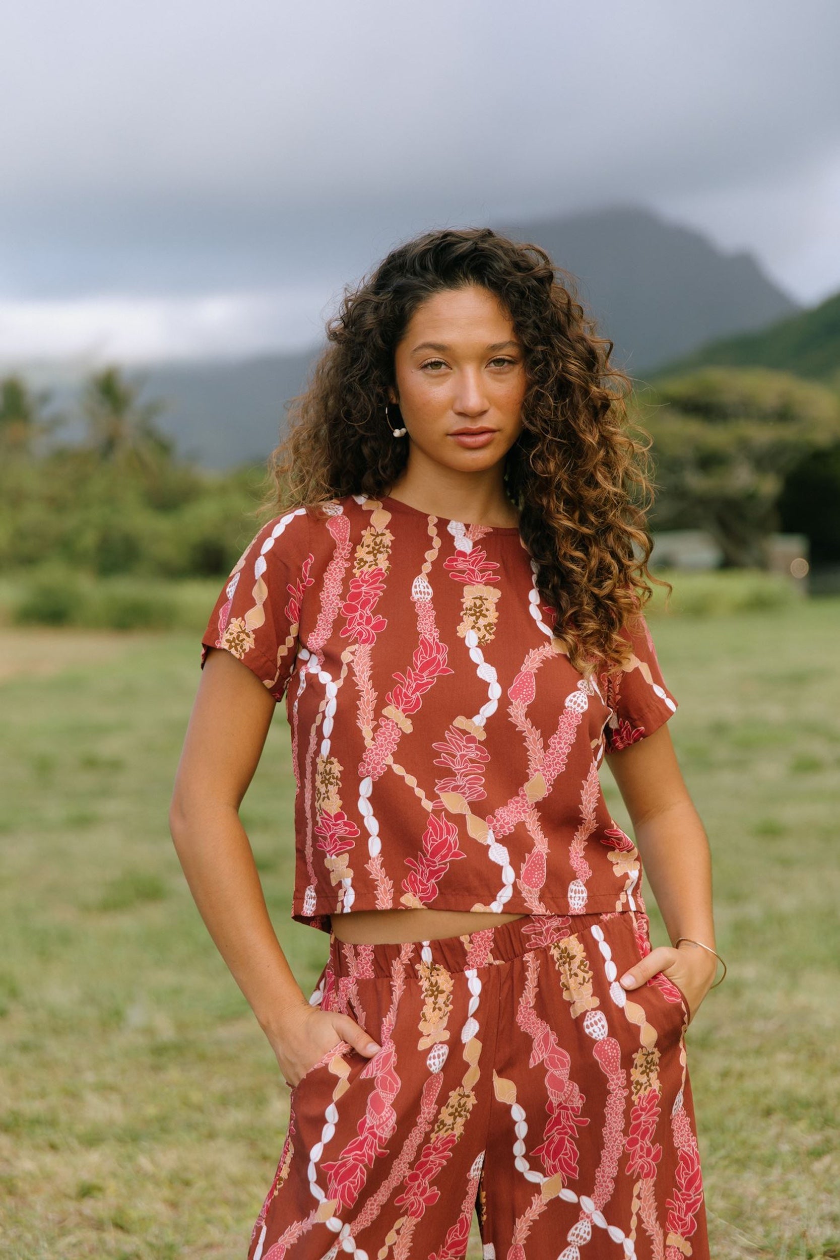 woman with brown hair wearing red-brown colored top with button closure back and lei print