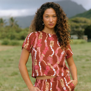 woman with brown hair wearing red-brown colored top with button closure back and lei print