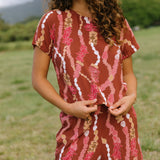 woman with brown hair wearing red-brown colored top with button closure back and lei print