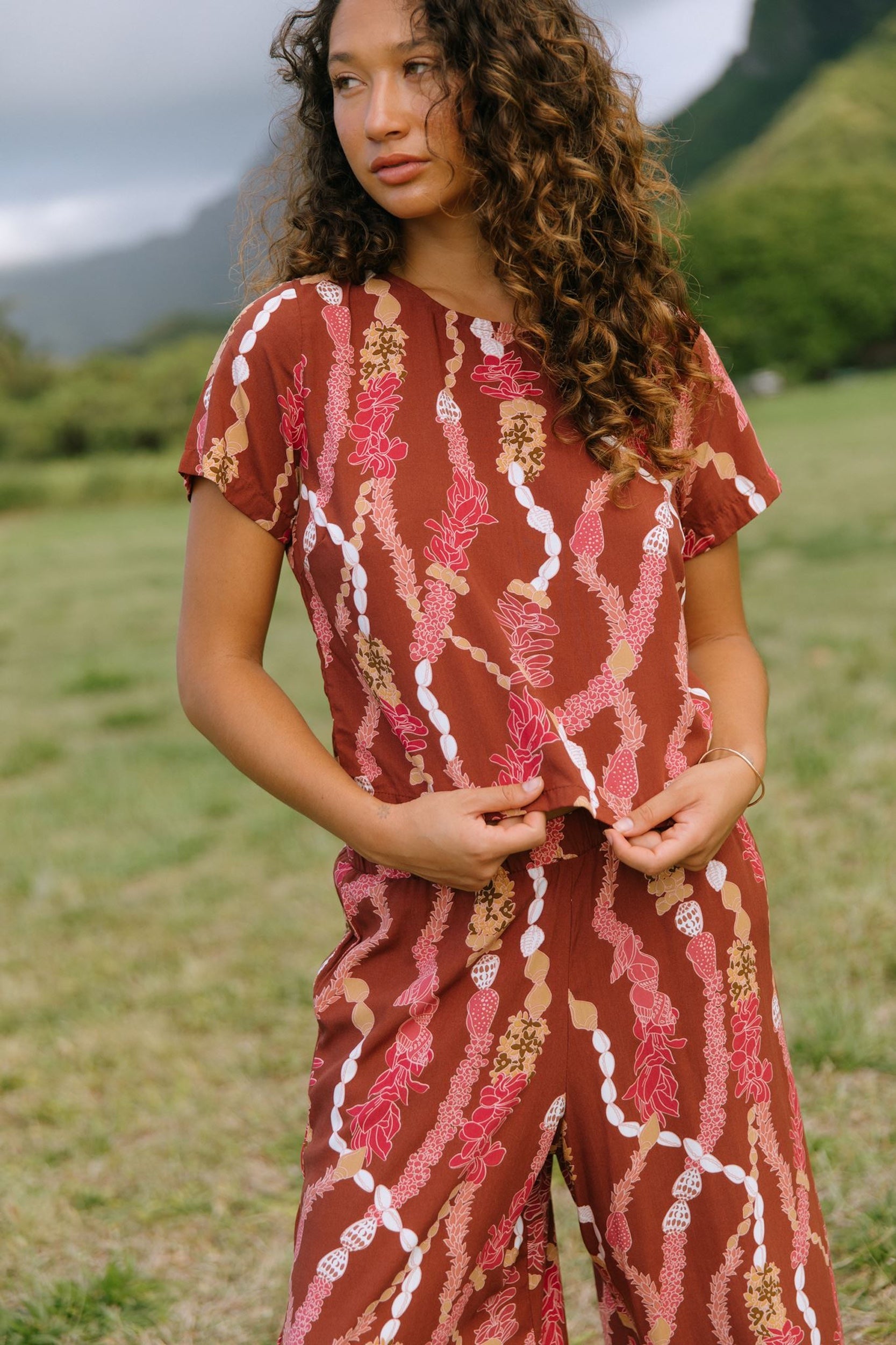 woman with brown hair wearing red-brown colored top with button closure back and lei print