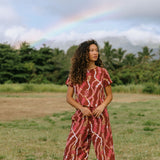 woman with brown hair wearing red-brown colored pant and top with button closure back and lei print