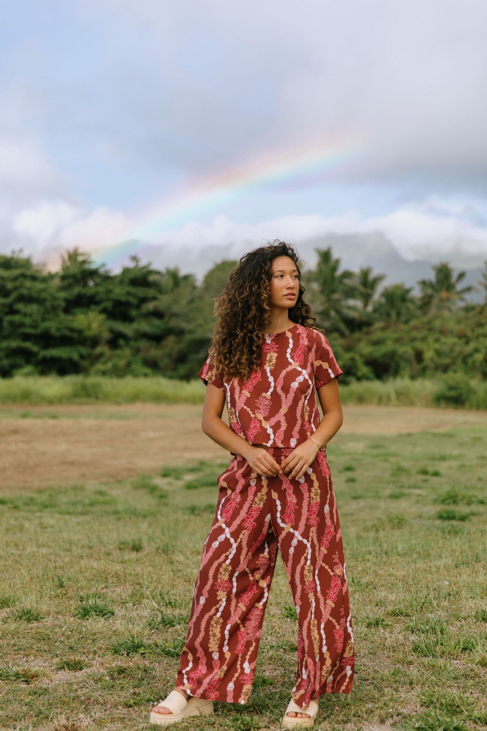 woman with brown hair wearing red-brown colored pant and top with button closure back and lei print