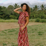 woman with brown hair wearing red-brown colored top with button closure back and lei print