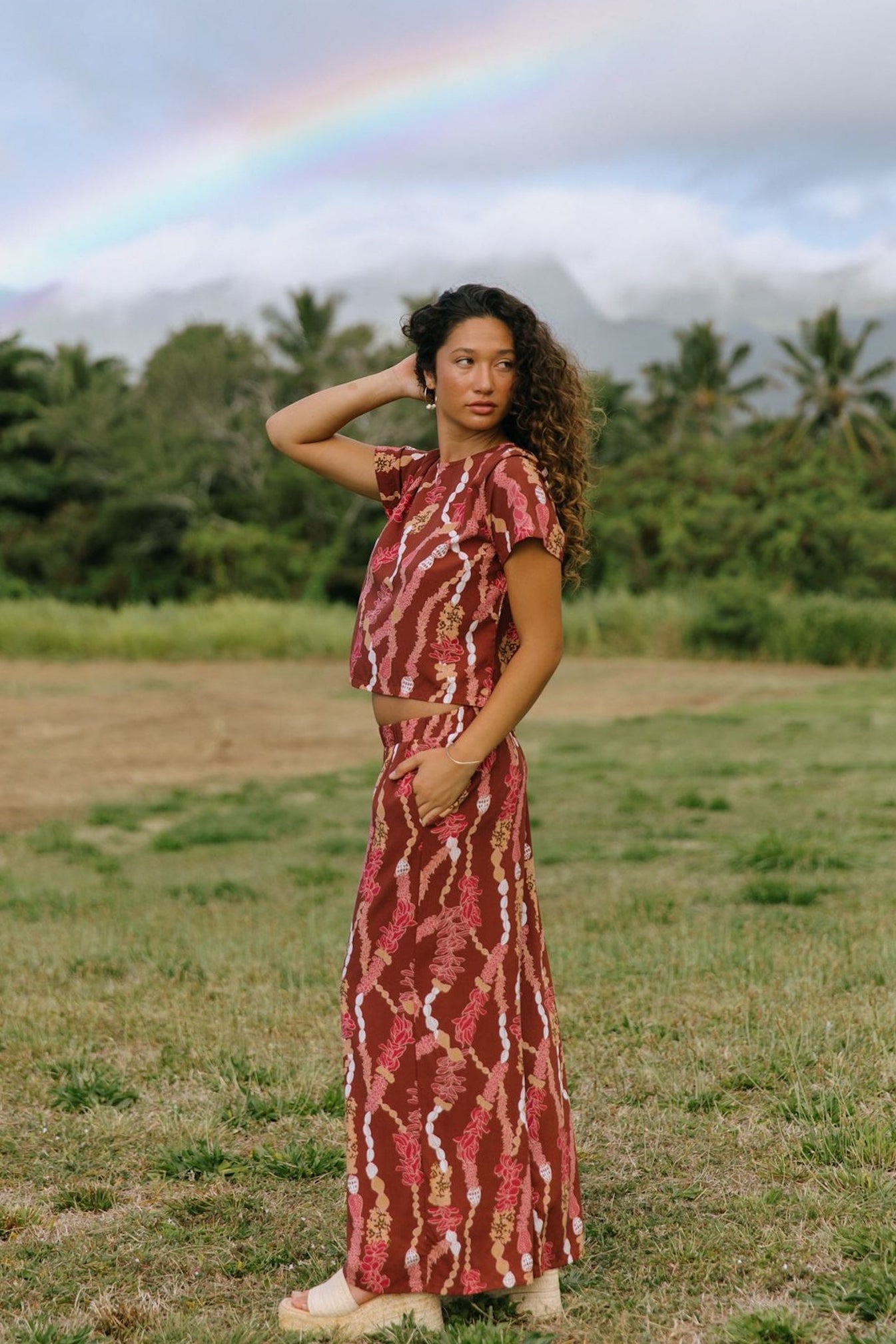 woman with brown hair wearing red-brown colored top with button closure back and lei print