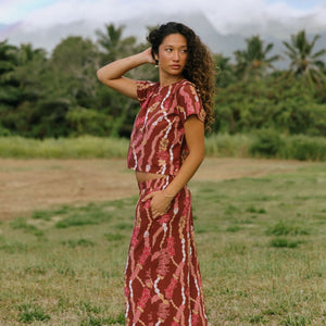woman with brown hair wearing red-brown colored top with button closure back and lei print