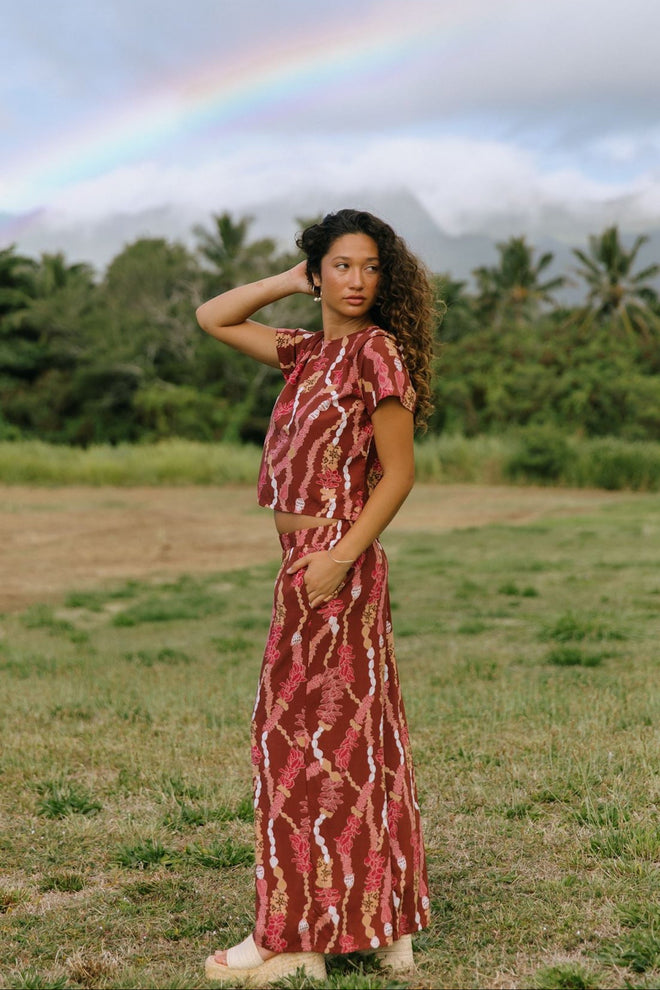 woman with brown hair wearing red-brown colored top with button closure back and lei print