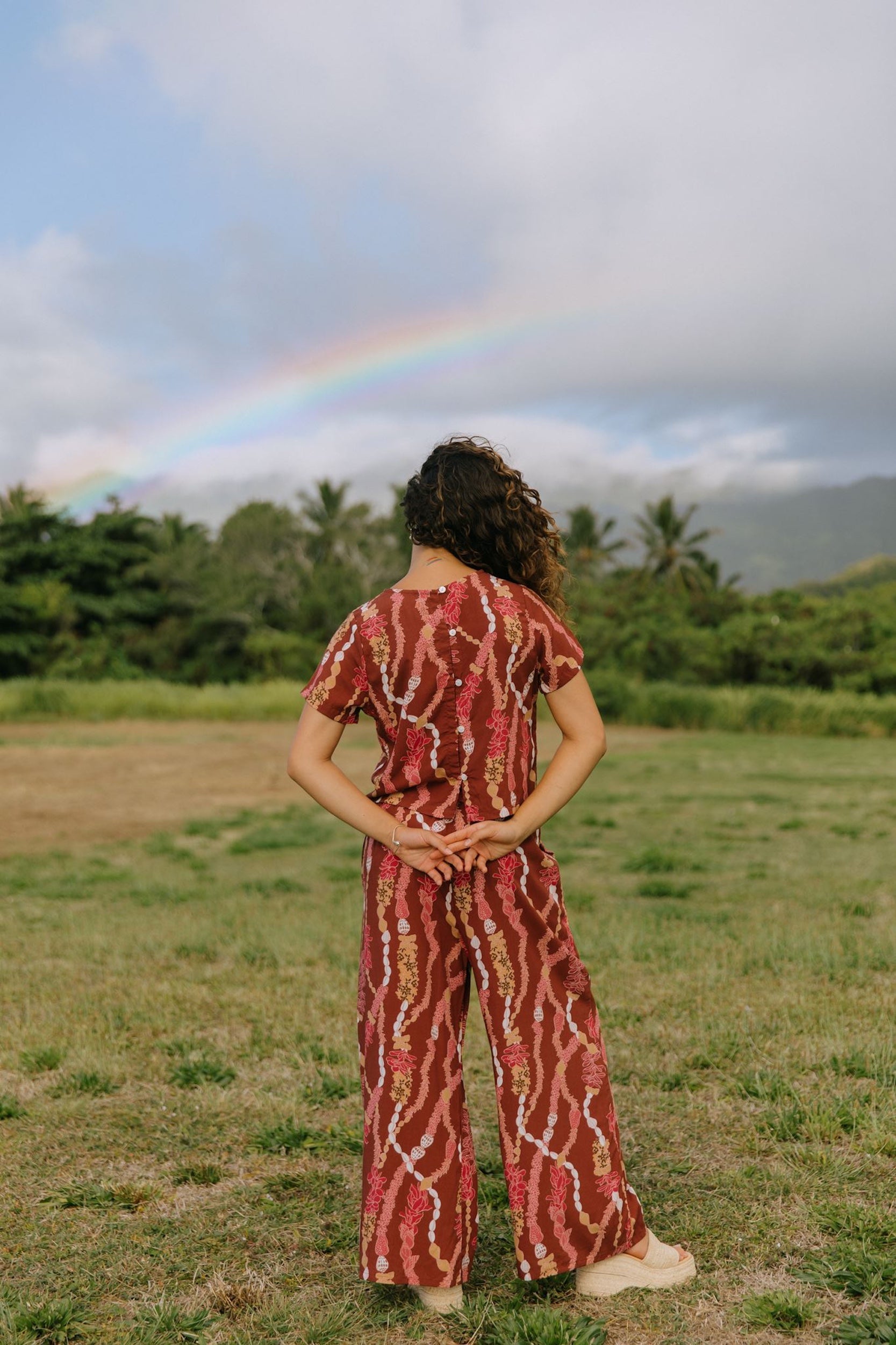 woman with brown hair wearing red-brown colored top with button closure back and lei print