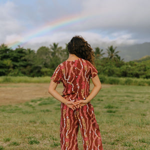 woman with brown hair wearing red-brown colored top with button closure back and lei print