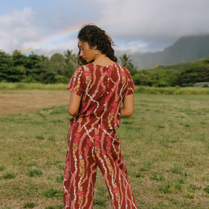 woman with brown hair wearing red-brown colored pant and top with button closure back and lei print