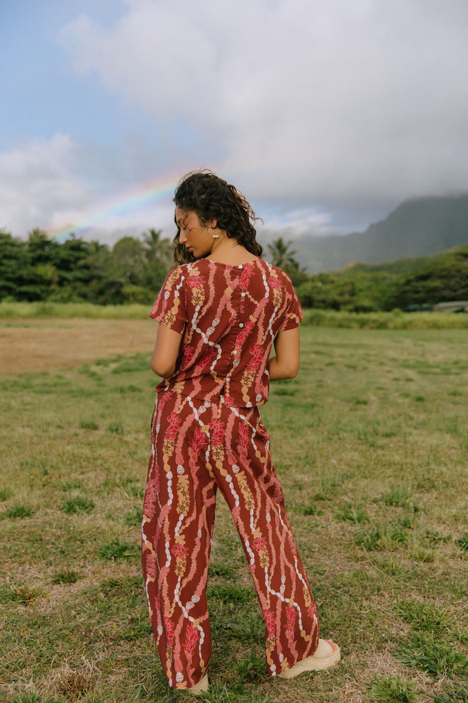 woman with brown hair wearing red-brown colored pant and top with button closure back and lei print
