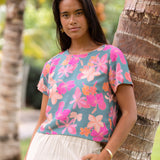 woman with brown hair wearing a teal t-shirt top with orange and pink foral print