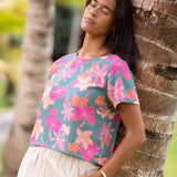 woman with brown hair wearing a teal t-shirt top with orange and pink foral print