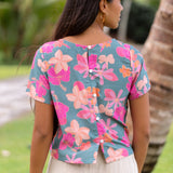 woman with brown hair wearing a teal t-shirt top with orange and pink foral print