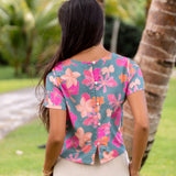 woman with brown hair wearing a teal t-shirt top with orange and pink foral print
