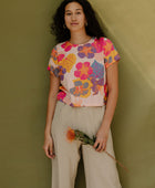 Woman wearing short sleeve tee with bright multi colored floral print on light pink ground.