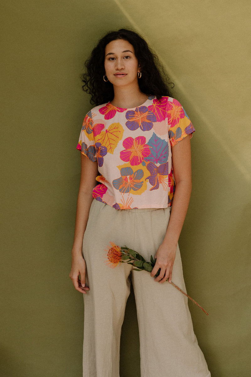 Woman wearing short sleeve tee with bright multi colored floral print on light pink ground.