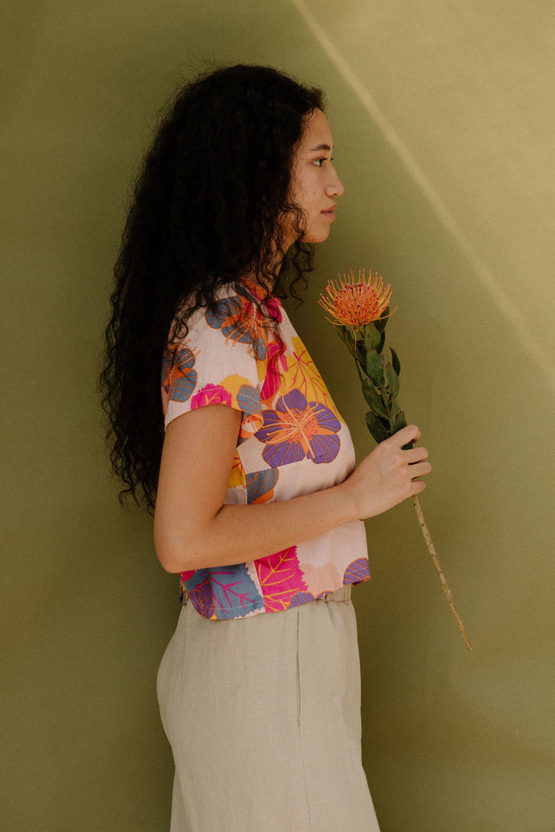 Woman wearing short sleeve tee with bright multi colored floral print on light pink ground.