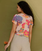 Woman wearing short sleeve tee with bright multi colored floral print on light pink ground.