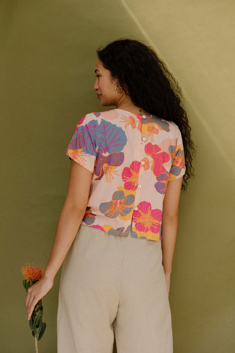 Woman wearing short sleeve tee with bright multi colored floral print on light pink ground.