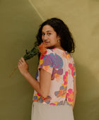 Woman wearing short sleeve tee with bright multi colored floral print on light pink ground.