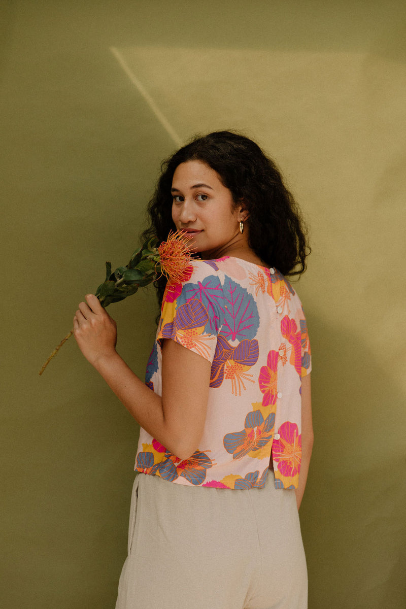 Woman wearing short sleeve tee with bright multi colored floral print on light pink ground.