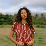 woman with brown hair wearing red-brown colored top with button closure back and lei print