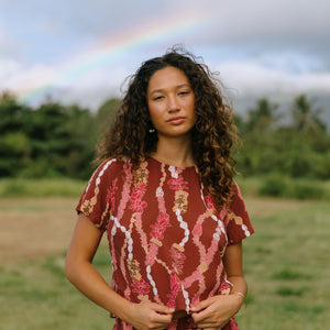 woman with brown hair wearing red-brown colored top with button closure back and lei print