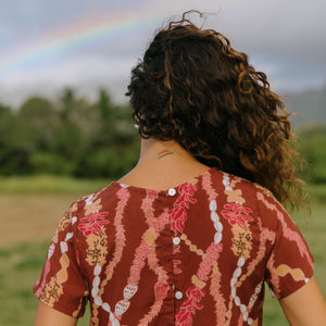 woman with brown hair wearing red-brown colored top with button closure back and lei print