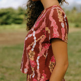 woman with brown hair wearing red-brown colored top with button closure back and lei print